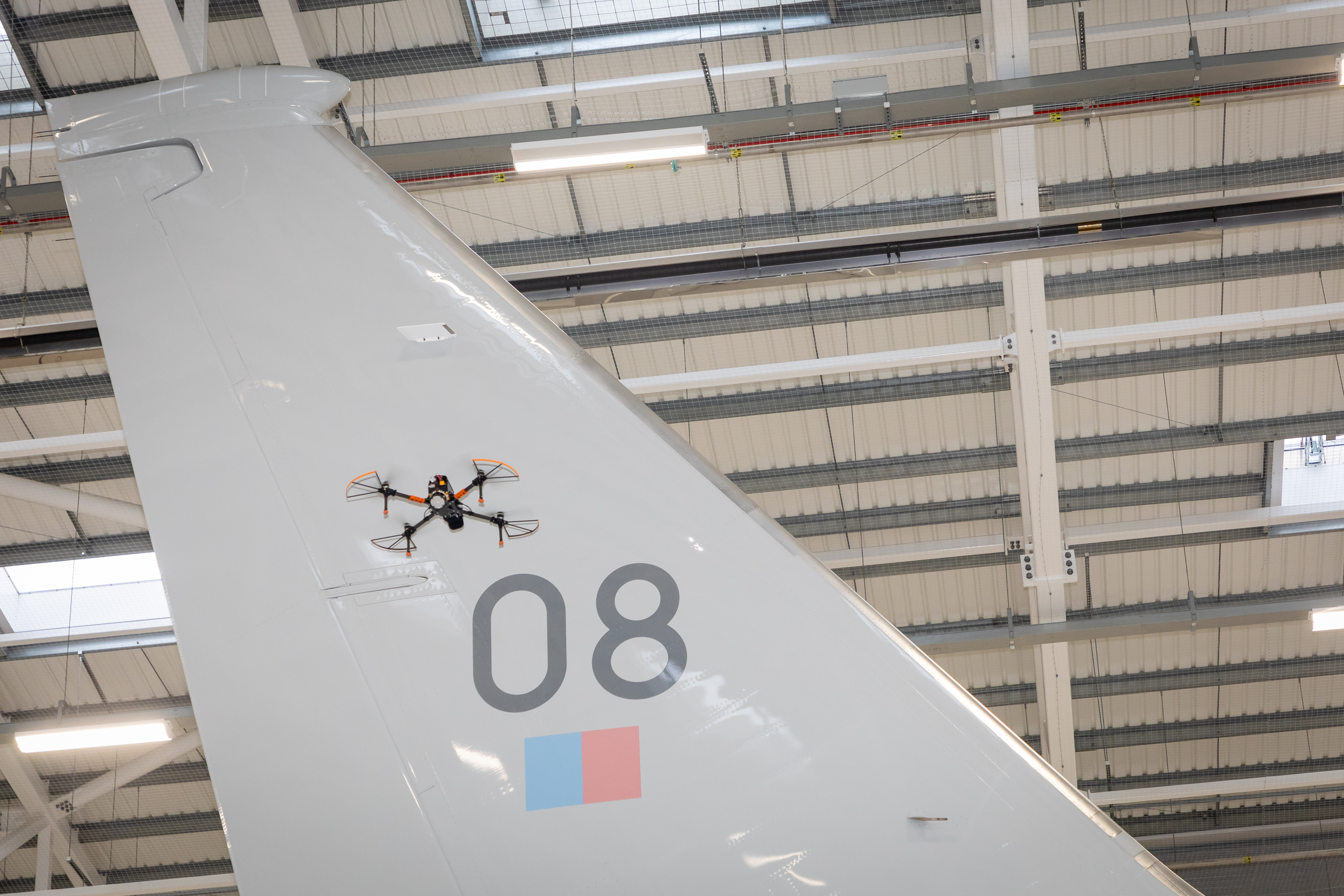 A drone flies in front of a tail fin of an aircraft in a hangar